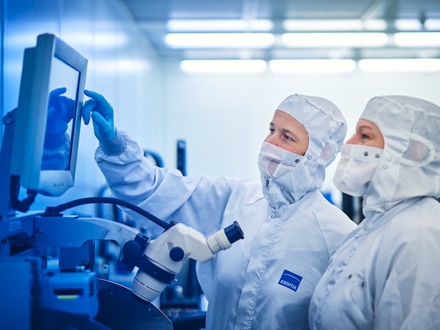 Two employees in cleanroom clothing looking at a screen