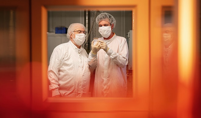 Two employees in a clean room looking at a lens