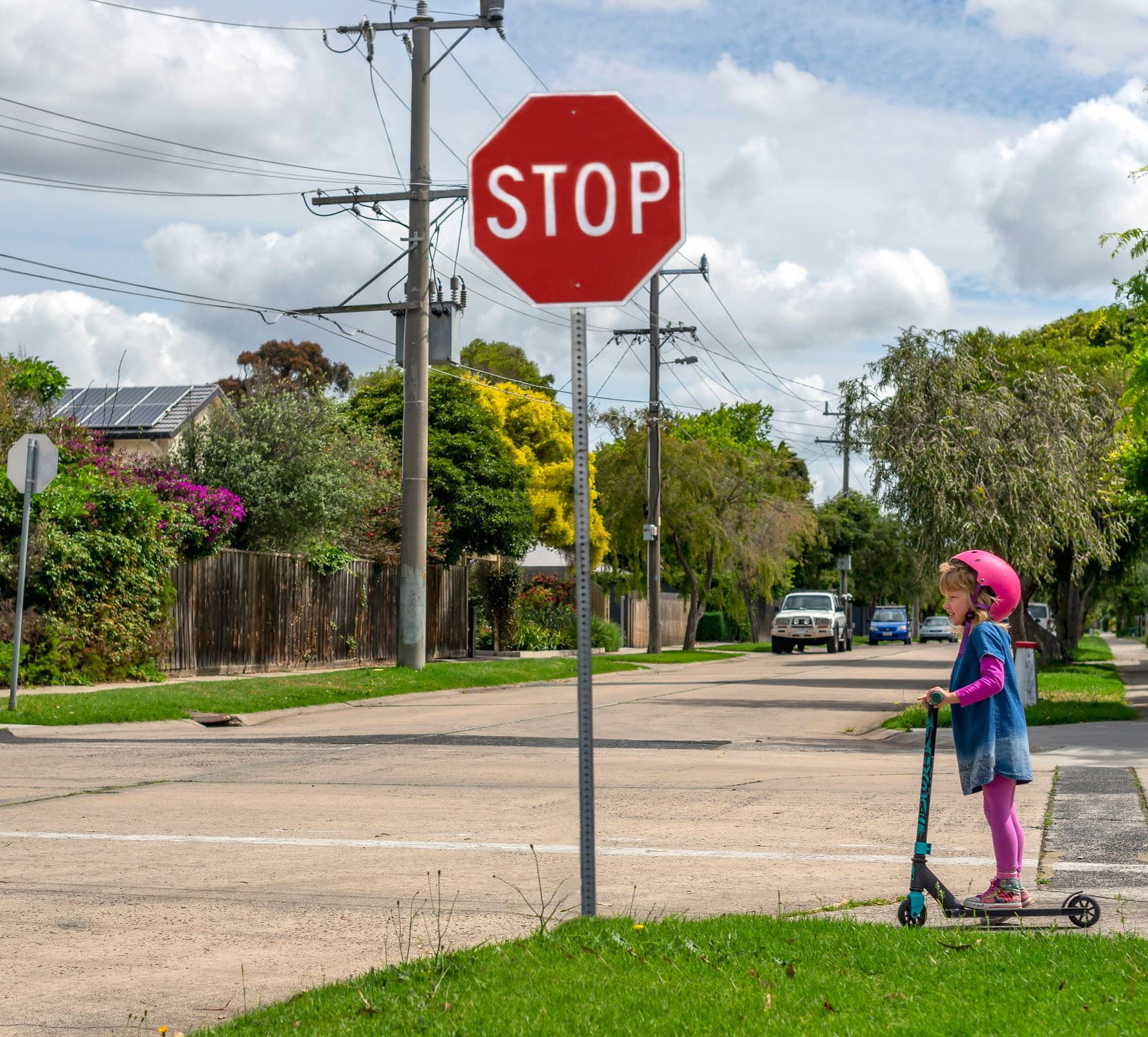 A little girl crosses the street on an e-scooter at a stop sign